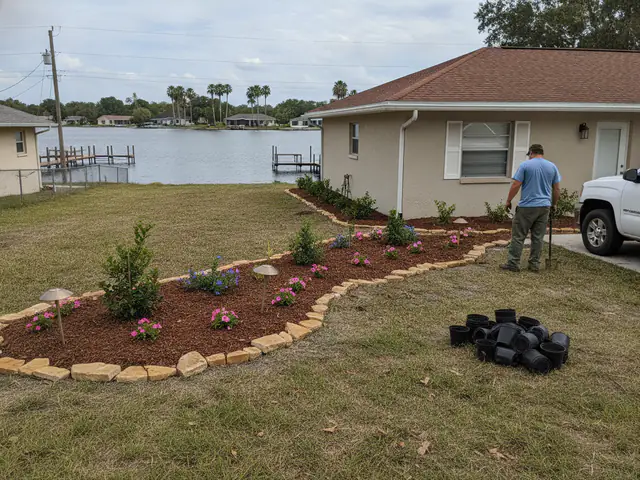 A newly planted front bed with young shrubs in fresh mulch, a stone border and path lights